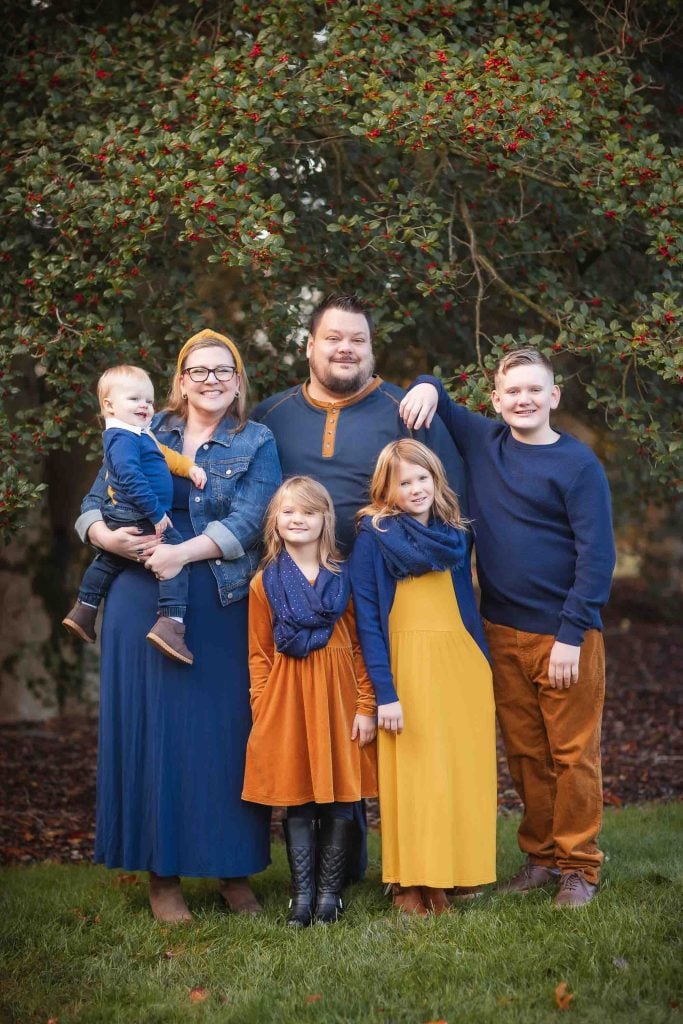 A family of six, with two adults and four children, posing outdoors under a tree with red berries, smiling for a Family Portrait.