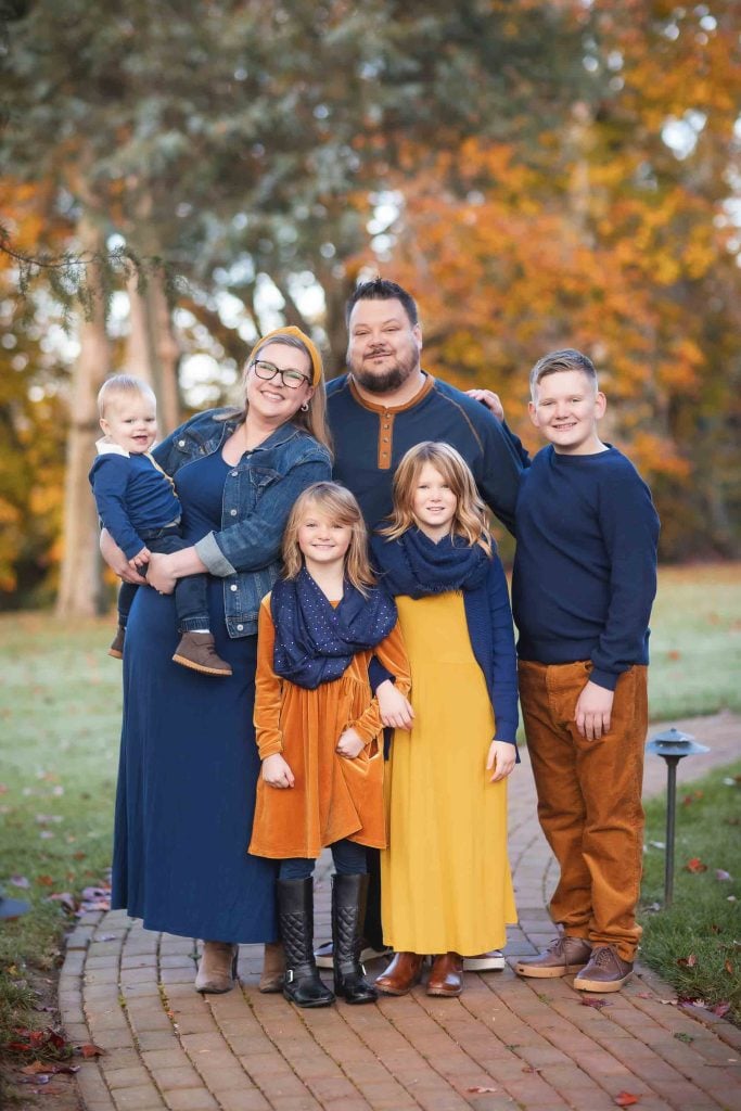 A Family Portraits session featuring two adults and four children posing happily in an autumnal park setting.