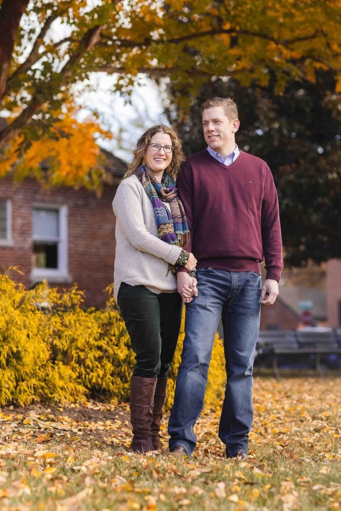 A couple holding hands in a park during autumn, surrounded by trees with colorful leaves and fallen leaves covering the ground, perfect for family portraits.