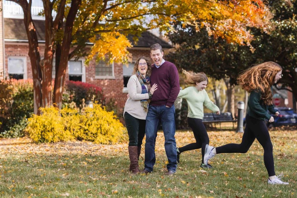 A family of four laughing and playing tag in a park with colorful autumn leaves in the background, perfect for Family Portraits.