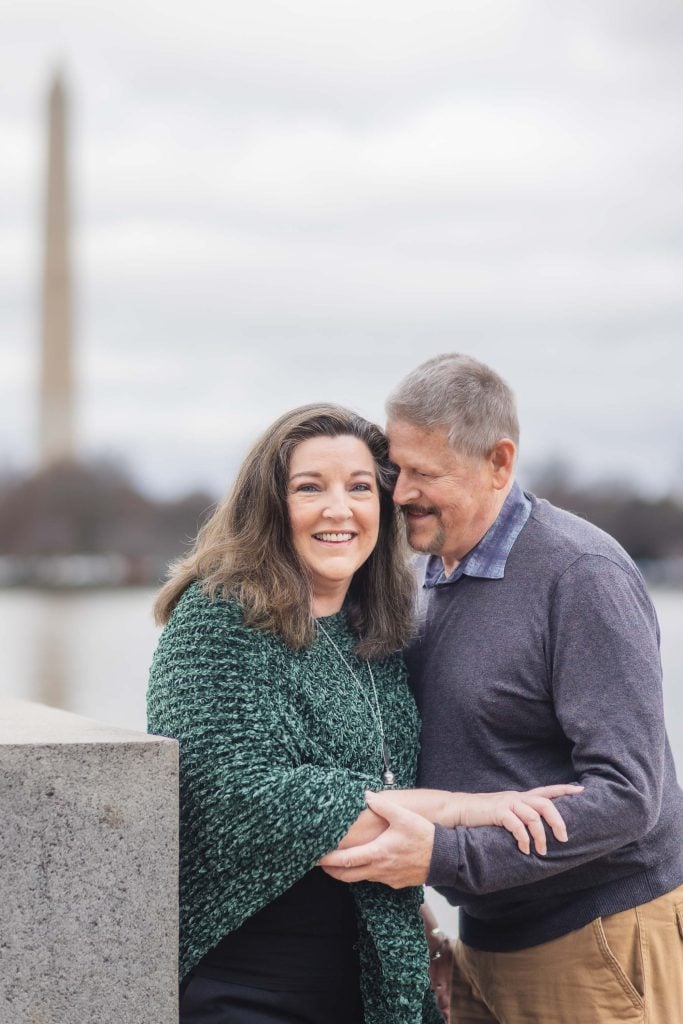 A woman and a man stand close together, smiling for family portraits, with the Washington Monument visible in the background.