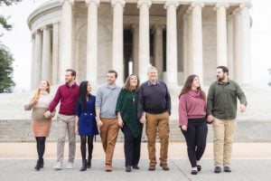 A family of seven walking hand in hand in front of the Jefferson Memorial, smiling and casually dressed.