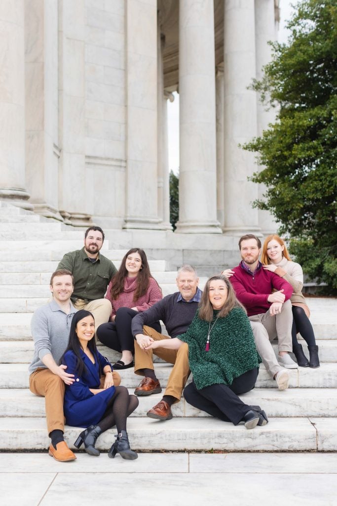 A family of nine people, seated on marble steps outside the Jefferson Memorial with its large columns, posing for a portrait.