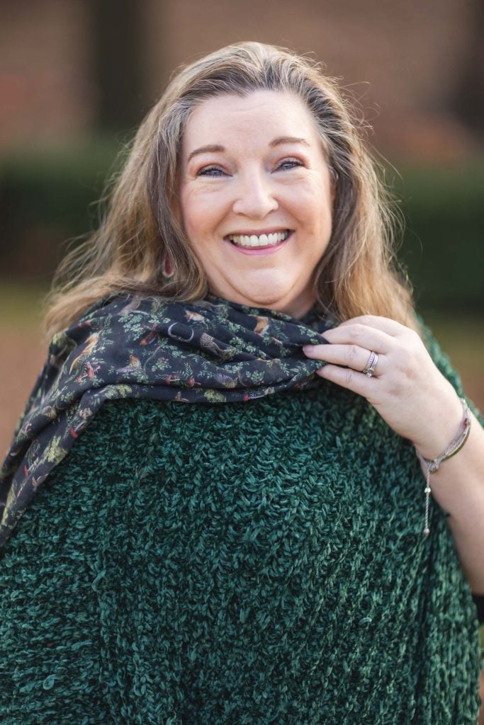 A woman smiling, standing outdoors with the Jefferson Memorial in the background, wearing a green textured top and a patterned scarf over her shoulder.