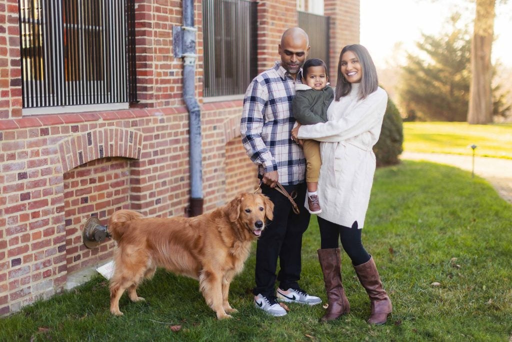 A family poses for a portrait with a Golden Retriever outside a brick building on a grassy lawn, capturing the joy of their lives.