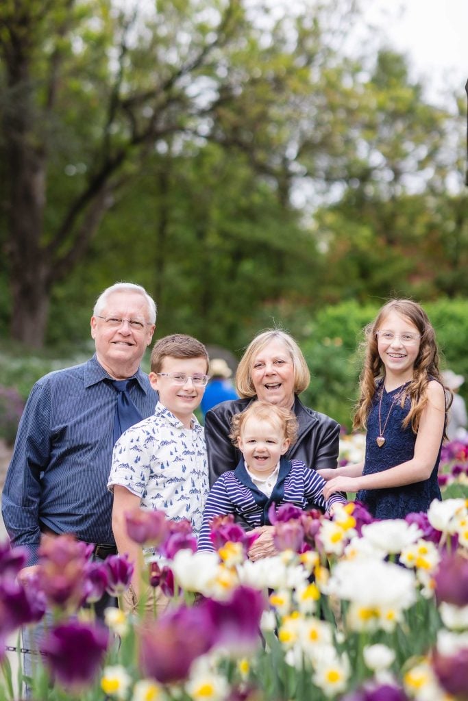 A group portrait of two adults and three children standing among colorful flowers with trees in the background at Brookside Gardens.