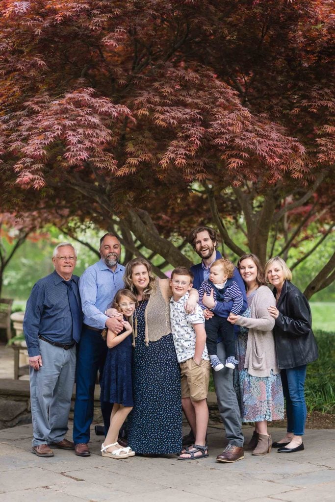 An extended family of nine, including adults and children, pose together under a redleafed tree at Brookside Gardens.