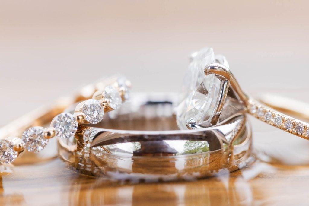 A closeup photo captures the intricate details of three wedding rings on a wooden surface at The Barns at Hamilton Station. Two rings showcase stunning diamond settings, while one is a simple, elegant band.