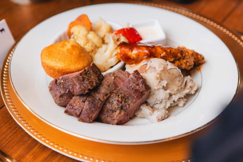 A beautifully arranged plate of food at The Barns at Hamilton Station features sliced beef, mashed potatoes, a muffin, roasted vegetables, and a piece of chicken with sauce—attention to detail perfect for a wedding.