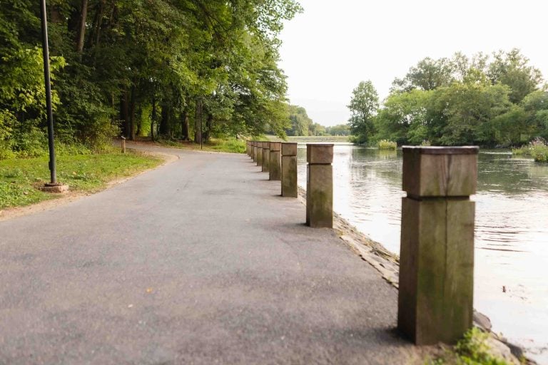 A riverside path lined with wooden posts and trees on the left offers a serene stroll beside the calm waters of Lake Elkhorn on the right.