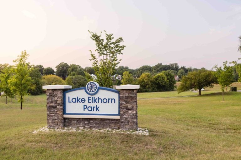 The stone sign, etched with "Lake Elkhorn Park," sits proudly on a grassy area, surrounded by a tranquil backdrop of trees.