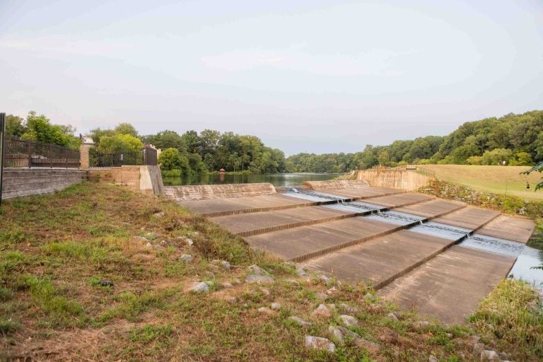 The concrete spillway at Lake Elkhorn, with water cascading gracefully, is flanked by grassy banks and trees under a cloudy sky.